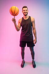 Young sportsman spinning basketball ball on finger - obrazy, fototapety, plakaty