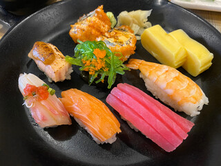 Top view of variety of sushi and rolls served on black plate. Plenty of nigiri, maki, and roll with tuna, salmon, shrimp and Tamagoyaki. Traditional Japanese food.