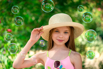 Stylish portrait of smiling girl in hat front of soap bubbles and green background. Summer season.