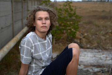 Portrait of a 15 year old teenage boy with curly hair in a deserted countryside in summer at sunset.