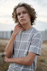 Portrait of a 15 year old teenage boy with curly hair in a deserted countryside in summer at sunset.