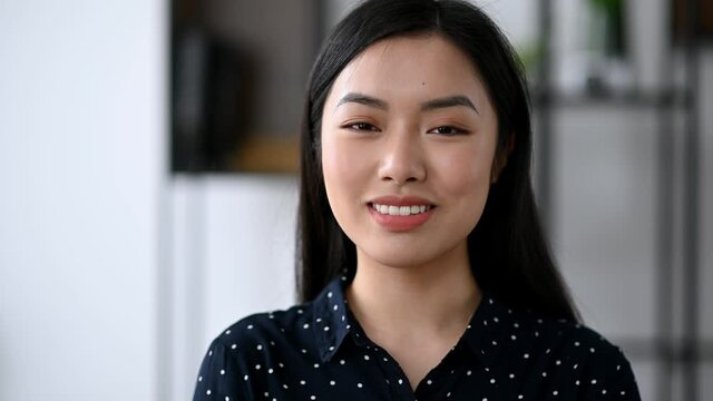 Close-up video portrait of attractive cute successful confident young brunette asian woman, office manager or student, in formal stylish shirt, looking directly at the camera, smiling friendly