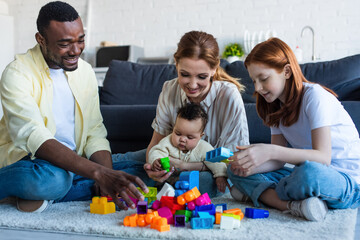 happy multicultural family playing with colorful building blocks on floor