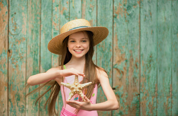 Stylish portrait of smiling little girl with starfish in hat front of green background. Summer season.