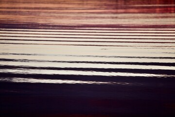 High-contrast shadows and bright reflections on the glowing water surface close-up. Bright ripples, abstract lines and pattern on colorful water surface. Abstract backgrounds and textures. Abstraction