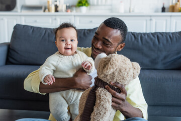 happy father holding cheerful african american baby girl and teddy bear