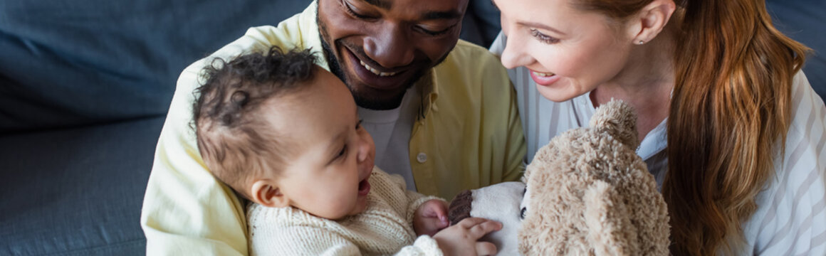 Happy Interracial Couple Looking At Cheerful Baby Touching Teddy Bear, Banner