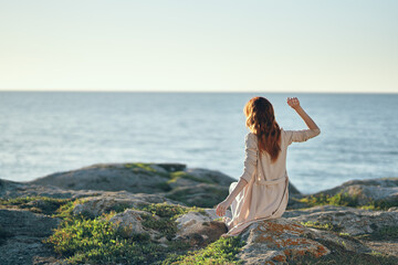 woman in sweaters with raised up hands on a stone near the sea in the mountains