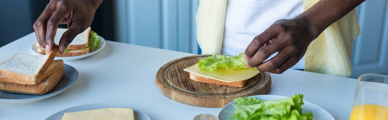 partial view of african american man making sandwiches with cheese and lettuce, banner