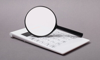 On a gray background, a black calculator and a magnifying glass with a place to insert text. Business concept