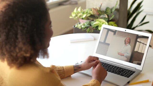 African-American female student studying online, using laptop computer for watching educational course, learning foreign language with a senior female tutor on the laptop screen, takes classes online