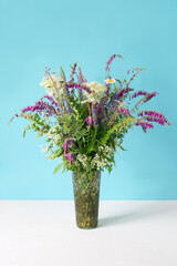 a lush bouquet of white and lilac wildflowers in a glass vase on a blue background