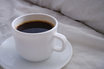 White cup of black coffee in a white bed.