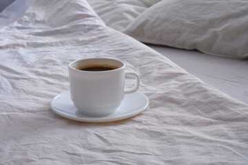 White cup of black coffee in a white bed.
