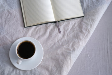 White cup of black coffee and a notebook in a white bed.