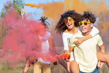 Beautiful young man and woman hold light up colored smoke bombs - Happy friends having fun in the...