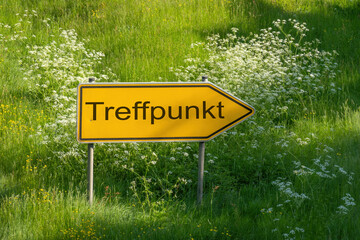 Gelbes Schild mit Aufschrift Treffpunkt als Wegweiser in Gr&uuml;ner Wiese mit weissen Blumen 