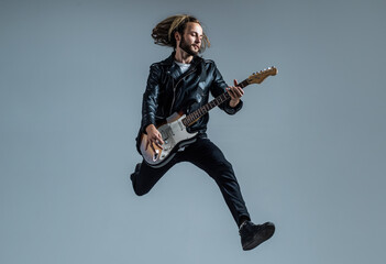 emotional bearded rock musician playing electric guitar in leather jacket and jumping, guitar player