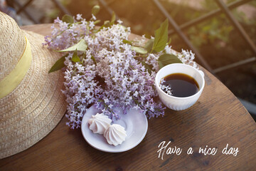 straw hat, coffee cup, lilac bouquet, meringue on a wooden table. have a nice day - text