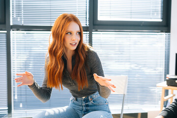 Close-up of attractive young redhead businesswoman talking and discussing new ideas with creative business team, during brainstorming of start-up projects in modern office room near window.