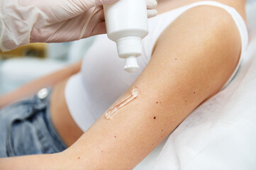 Close-up shot of squeezed transparent anesthetic gel for laser epilation procedure from a white container on female hand in spa salon