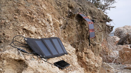 Solar panels charge a smartphone and batteries on an earthen slope near the sea