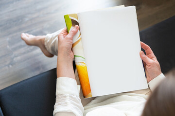beautiful female hands holding white magazine with blank cover mock up at home