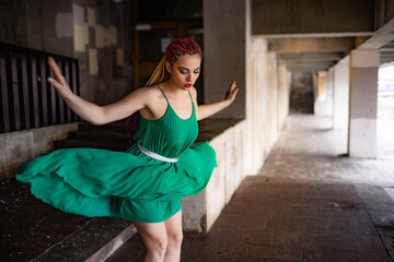 A girl with bright braids and glitter colored makeup in a bright green spring dress jumps off the steps of an old building