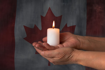 Hands with a candle on the background of the flag of Canada. In memory of the victims.