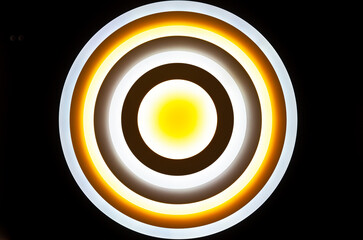 Modern round bright high-tech chandelier on the black ceiling and shines, close-up.