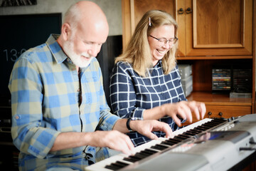 Cheerful senior couple playing piano four hands at home