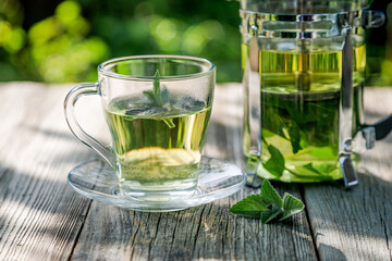 A cup of mint tea on a wooden table in the summer garden