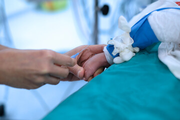 Doctor holding baby’s foot and injecting with needle to baby’s foot for drawing blood sample in cardiac operating room
