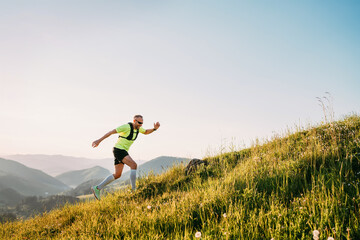 Middle-aged mountain trail runner man dressed bright t-shirt with a backpack in sports sunglasses...