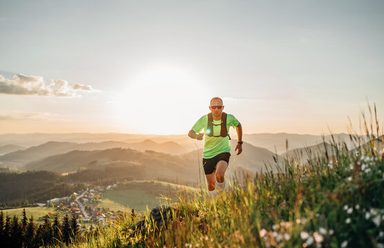 Active mountain trail runner dressed bright t-shirt with backpack in sport sunglasses running endurance marathon race by picturesque hills at sunset time. Sporty active people concept image.