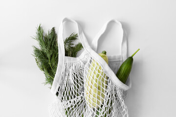 White mesh bag, vegetables flat lay on white background top view. Eco friendly, reusable shopping bag. Dill, zucchini, cucumber in cotton knitted string bag. Zero waste concept.