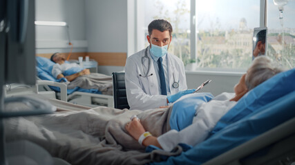 Hospital Ward: Friendly Doctor Wearing Face Mask Talks to Beautiful Senior Female Patient Resting in Bed, Explains Test Results, Gives Recovery Advice. Physician and Old Lady Recovering after Covid-19