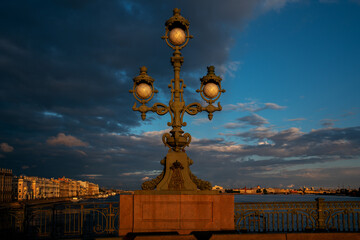 The lantern of the Trinity Bridge and the view of the spit of Vasilievsky Island and the Palace Embankment in the background in the first rays of the sun, St. Petersburg, Russia