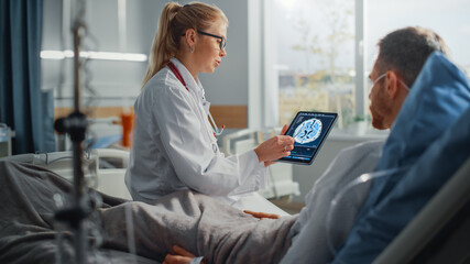 Hospital Ward: Friendly Female Doctor Talks to Sick Male Patient Resting in Bed, Uses Tablet...