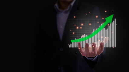 Business growth, progress or success concept. Businessman is showing hologram stock market investment profit report graph in bar chart on his hand with green arrow point up in dark background.