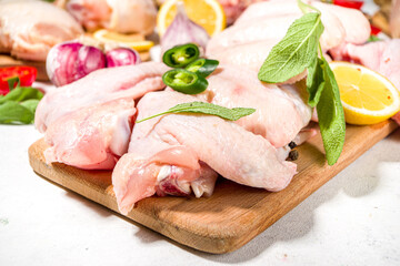 Various raw chicken meat portions. Set of uncooked chicken fillet, thigh, wings, strips and legs on white cooking table background with spices