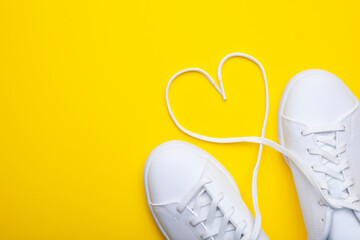 Pair of casual shoes with heart shaped laces on yellow background. Top view of stylish sneakers on color background with place for text - obrazy, fototapety, plakaty