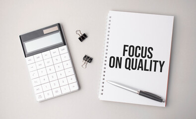 The word Focus on Quality a is written on a white background next to a pen ,calculator and reports. Business concept