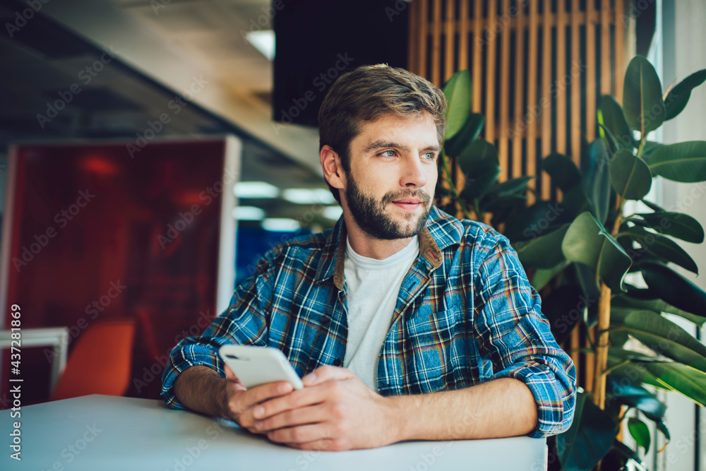 Poster contemplative male blogger with digital mobile technology sitting at coworking table and thinking ab