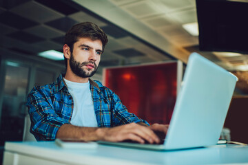 Caucasian male programmer creating software system via laptop application using coworking wifi...