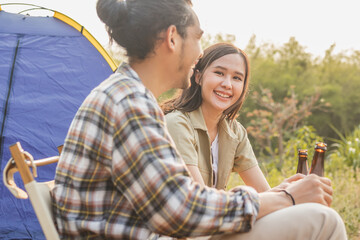 Enjoy asian young woman, girl and man cheering with beer bottle, sitting on chair . Adventure couple, people camping in forest. Eco activity, lifestyle nature on holiday concept.