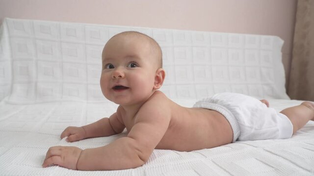 A playful newborn is lying on the bed on his stomach and smiling. Happy baby
