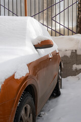 Side of a red car covered with snow. Closeup view in winter time.