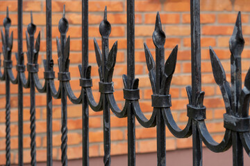 Black metal fence closeup against brick wall. Selective focus. Background image.