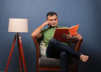 indian middle aged man reading book on sofa